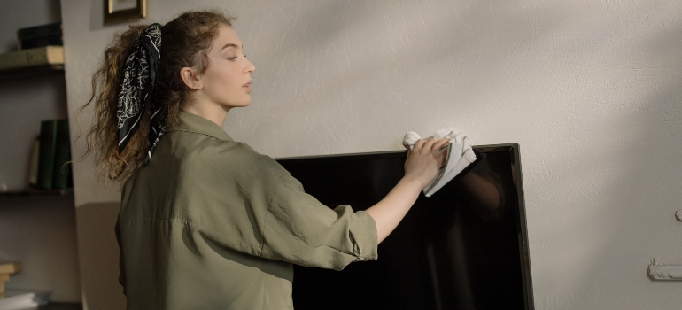 A woman in gray shirt cleaning the TV.