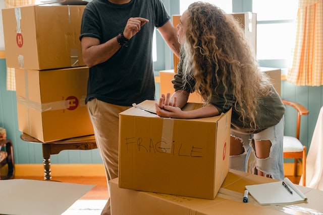 A woman and a man standing next to a box with fragile writing on it
