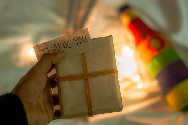 A person's hand holding a gift box and a thank-you card