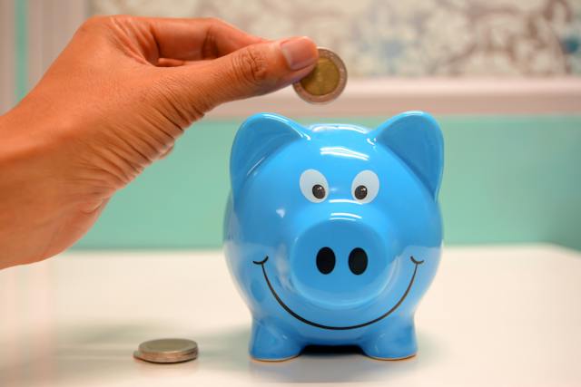 Person putting coins in a blue piggy bank
